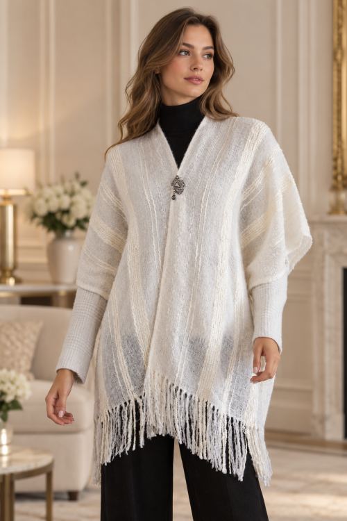 Damenponcho in Cremeweiß mit strukturiertem Strickmuster und Fransen, kombiniert mit schwarzem Rollkragenpullover und schwarzer Hose.