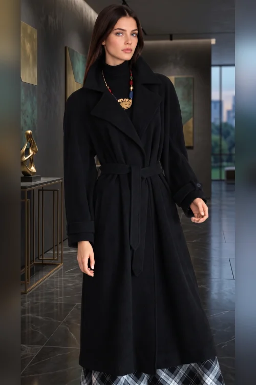 Lange schwarzer Damenmantel mit breitem Reverskragen und Bindegürtel, kombiniert mit einem schwarzen Rollkragenpullover und einem schwarz-grau karierten Rock.